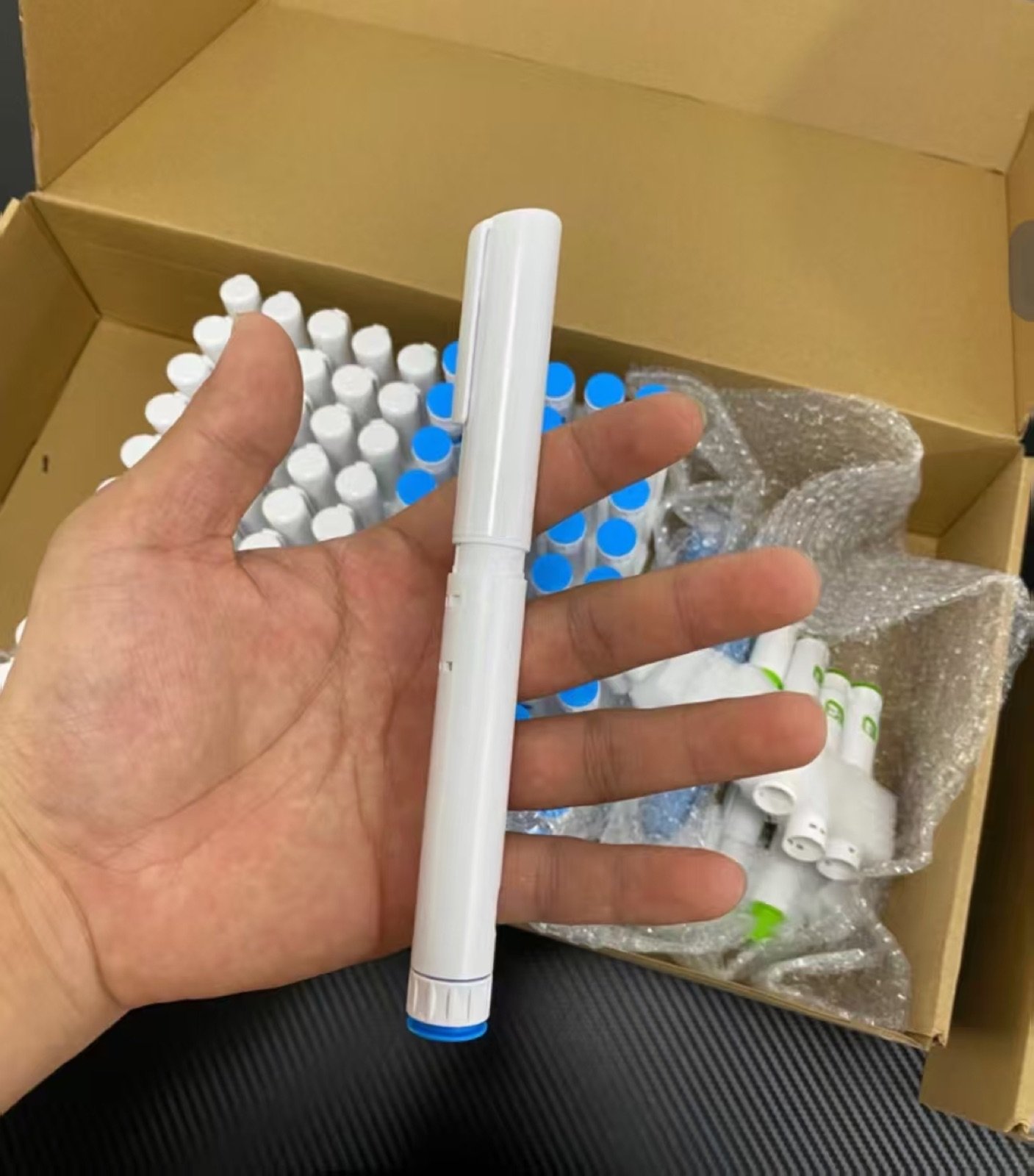 White plastic pen injector sample held beside packed samples
